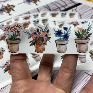 May include: Four potted flower stickers with a white background. The flowers are painted in a watercolor style with a variety of colors, including red, yellow, blue, and green. The pots are brown and have a white rim.