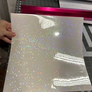 May include: A sheet of iridescent holographic vinyl with a white background and a scattered pattern of small, iridescent triangles.