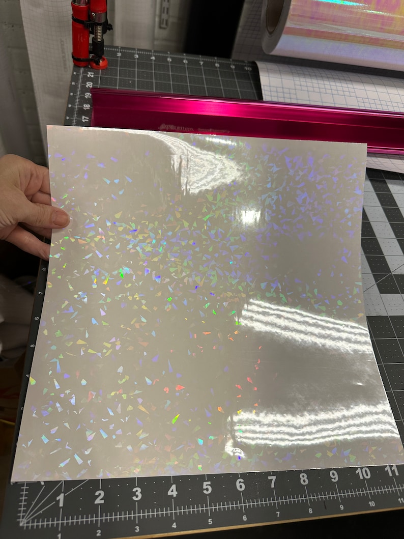 May include: A sheet of iridescent holographic vinyl with a white background and a scattered pattern of small, iridescent triangles.