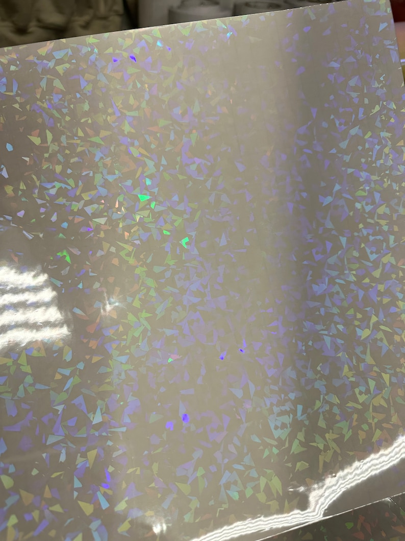 May include: A sheet of iridescent holographic vinyl with a white background and a pattern of small, randomly placed, iridescent triangles.