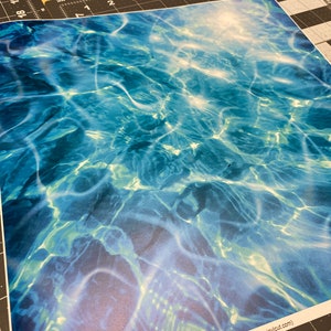 May include: Abstract blue and green water ripple pattern with a white, light blue, and green gradient. The pattern is reminiscent of the surface of a pool or ocean.