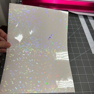 May include: A sheet of iridescent white vinyl with a holographic finish. The vinyl has a scattered pattern of small, iridescent triangles.