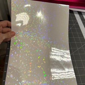 May include: A sheet of iridescent white vinyl with a holographic finish. The vinyl has a scattered pattern of small, iridescent triangles.