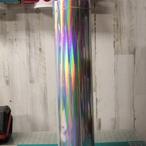 May include: A roll of iridescent holographic vinyl film on a black stand. The film is wrapped around a cardboard tube and has a rainbow sheen.