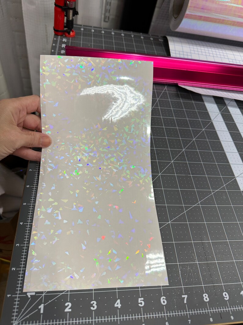 May include: A sheet of iridescent white vinyl with a holographic finish. The vinyl has a scattered pattern of small, iridescent triangles.