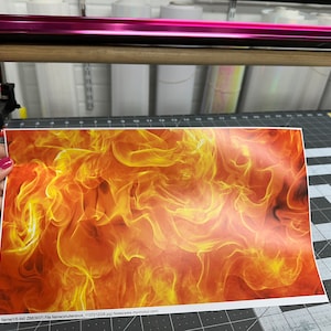 May include: A close-up of a printed sheet of orange, yellow, and red flames. The sheet is being held by a hand.