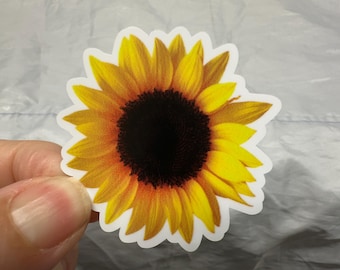 May include: A sticker featuring a detailed sunflower with yellow petals and a dark brown center. The sunflower is set against a white background, creating a vibrant and eye-catching design. Perfect for decorating laptops, water bottles, or notebooks.
