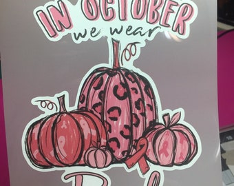 May include: A pink and white graphic with the text "IN OCTOBER we wear Pink". The design features several pumpkins, including one with a leopard print pattern, and a pink ribbon.