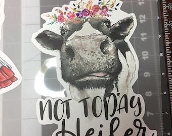 May include: A sticker featuring a black and white cow with a floral crown. The cow has a watercolor effect. The text "NOT TODAY Heifer" is written in a black script font below the cow's face.