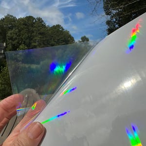 May include: A sheet of iridescent holographic vinyl with a rainbow effect. The vinyl is being peeled back to reveal the adhesive side.