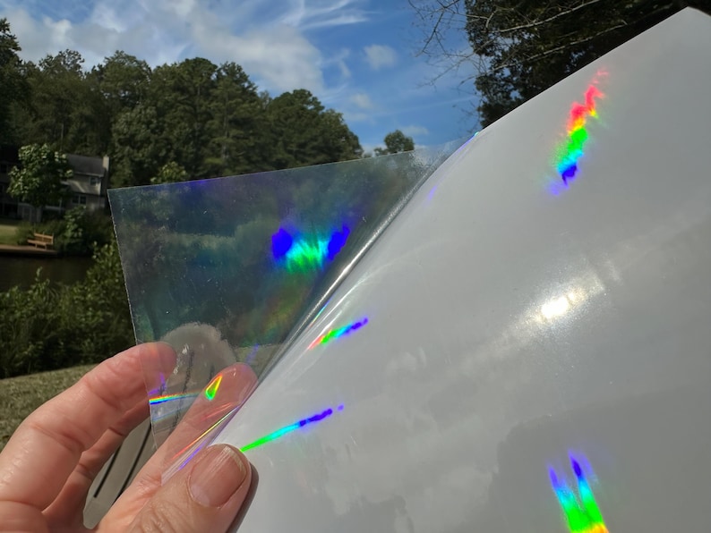 May include: A sheet of iridescent holographic vinyl with a rainbow effect. The vinyl is being peeled back to reveal the adhesive side.