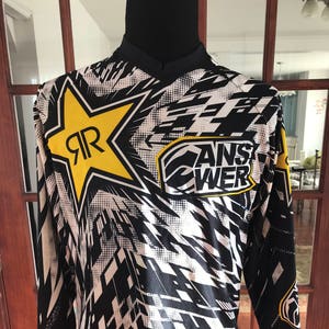 May include: Black and white long-sleeved shirt with a yellow star and the text "Answer" in a white circle. The star has the letter "R" inside it.