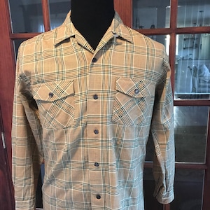 Pode incluir: Uma camisa de manga comprida xadrez com colarinho de botões e dois bolsos no peito. A camisa é marrom, bege e verde.