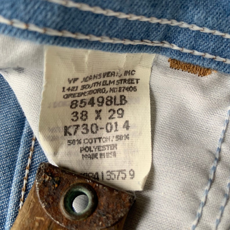 May include: A white tag with black text, VF Jeanswear Inc, 1421 South Elm Street, Greensboro, NC 27405, 85498LB, 38 x 29, K730-014, 50% Cotton/50% Polyester, Made in USA, 4135759.