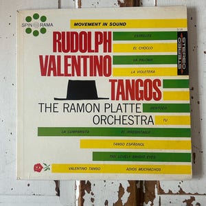 May include: Vintage vinyl record album cover for "Rudolph Valentino Tangos" by The Ramon Platte Orchestra. The cover features a hat illustration and text in red, yellow, and green on a white background. The album is labeled "Stereo".