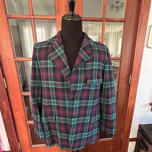 May include: A green, red, and black plaid blazer with a button closure. The blazer has two pockets on the front and a single button on each cuff.