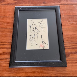 Peut inclure: Une estampe encadrée en noir d'un dessin à l'encre noire et blanche de deux personnages debout sous un arbre. Le dessin est sur du papier crème et porte un tampon rouge dans le coin inférieur droit.