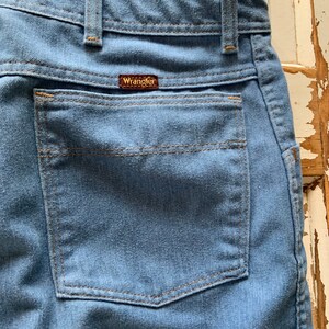 May include: A close-up of a blue denim back pocket with a brown leather Wrangler label.
