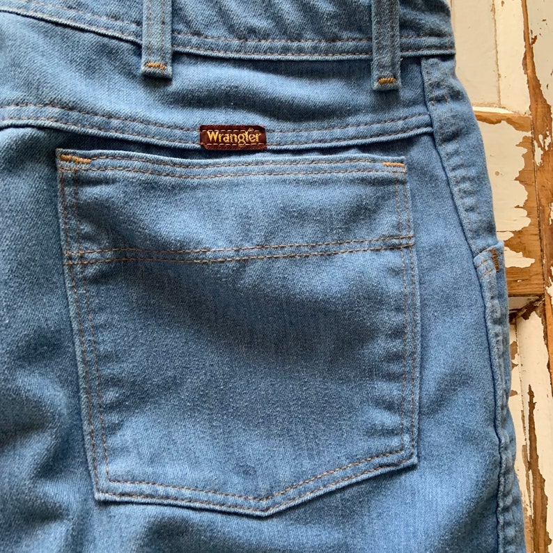 May include: A close-up of a blue denim back pocket with a brown leather Wrangler label.