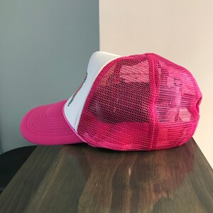 Op de afbeelding: Roze en witte truckercap met een mesh achterkant. De pet heeft een klein geborduurd ontwerp aan de voorkant.