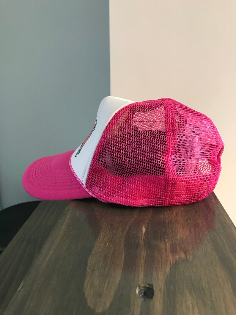 Op de afbeelding: Roze en witte truckercap met een mesh achterkant. De pet heeft een klein geborduurd ontwerp aan de voorkant.
