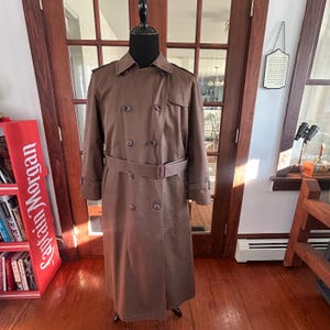 Puede incluir: Un abrigo tipo gabardina marr&oacute;n con dise&ntilde;o cruzado, cintur&oacute;n y botones. El abrigo se exhibe en un maniqu&iacute;. Es un estilo cl&aacute;sico, adecuado para diversas ocasiones.
