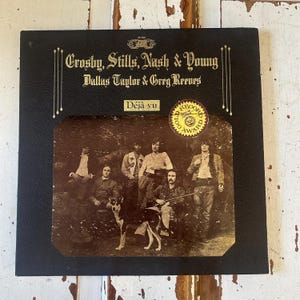 Könnte beinhalten: Ein Vintage-Vinyl-Schallplattenalbum von Crosby, Stills, Nash & Young mit dem Titel "Déjà Vu". Das Albumcover zeigt eine Sepia-Fotografie der Band mit einem Hund. Auf dem Cover ist ein Gold Record Award-Aufkleber angebracht.