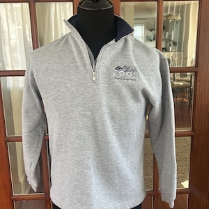 Peut inclure: Un sweat-shirt gris avec un col bleu marine et une fermeture éclair quart de zip. Le texte "2003 Walt Disney World" est affiché en bleu et blanc sur la poitrine. Le haut à manches longues est présenté sur un mannequin.