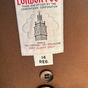 Puede incluir: Primer plano de un abrigo marr&oacute;n London Fog. La etiqueta dice "LONDON FOG" y "MADE AND STYLED BY THE LONDONTOWN CORPORATION". La etiqueta tambi&eacute;n indica que la cubierta es 70% algod&oacute;n y 30% poli&eacute;ster. La etiqueta de talla dice "14 REG."