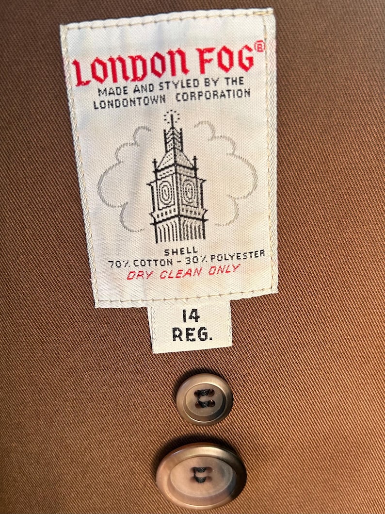Puede incluir: Primer plano de un abrigo marr&oacute;n London Fog. La etiqueta dice "LONDON FOG" y "MADE AND STYLED BY THE LONDONTOWN CORPORATION". La etiqueta tambi&eacute;n indica que la cubierta es 70% algod&oacute;n y 30% poli&eacute;ster. La etiqueta de talla dice "14 REG."