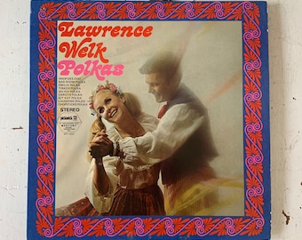 May include: A vintage vinyl record album cover featuring a couple in traditional folk attire dancing. The album is titled "Lawrence Welk Polkas" and features a red, white, and blue color scheme with a decorative border.