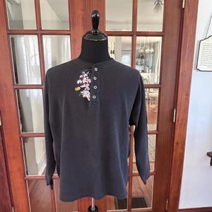 Puede incluir: Una camisa de manga larga gris oscuro con cuello abotonado y un gráfico de dibujos animados de Bugs Bunny y Piolín en la parte delantera.