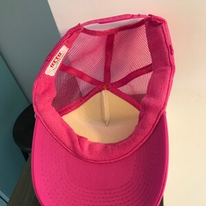 Op de afbeelding: Roze mesh trucker cap met een wit label waarop "OTTO" in rode letters staat. De pet heeft een klittenbandsluiting.