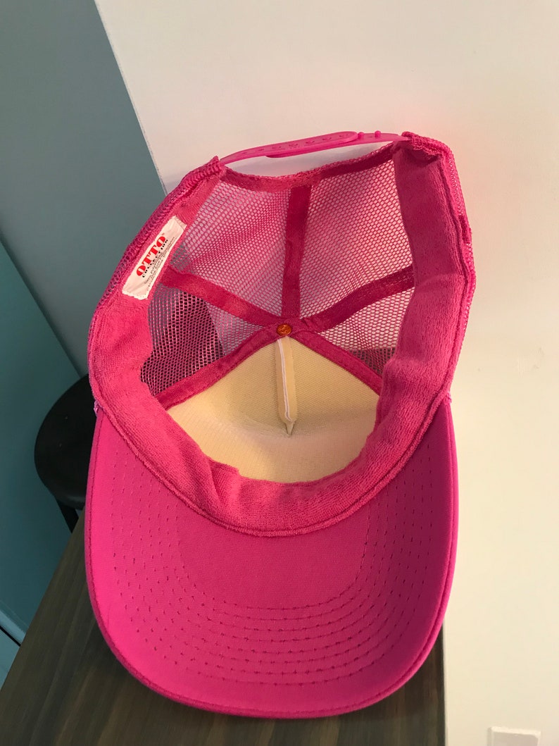 Op de afbeelding: Roze mesh trucker cap met een wit label waarop "OTTO" in rode letters staat. De pet heeft een klittenbandsluiting.