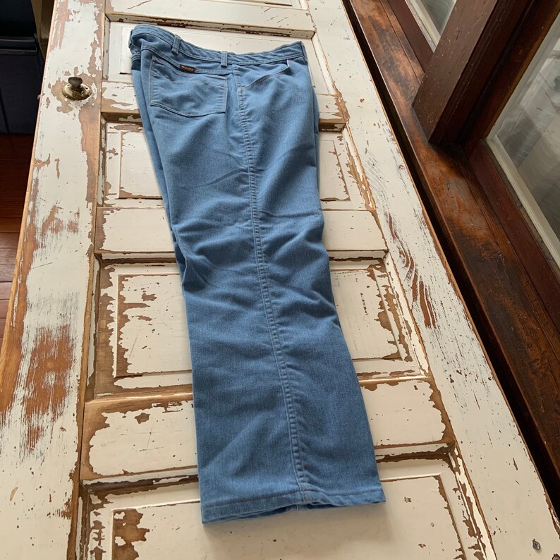 May include: A pair of blue denim pants with a straight leg fit. The pants have a brown leather patch on the back waistband with the brand name.