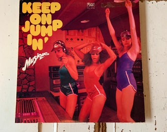 May include: A vinyl record cover featuring three women in colourful outfits dancing in a recording studio. The cover art is red and features the text "Keep On Jumpin' Musique".
