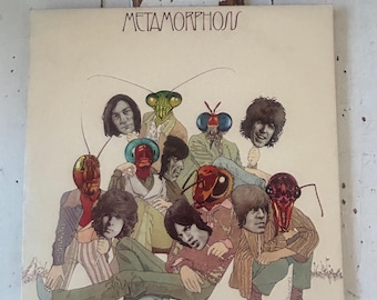 May include: A vintage vinyl record album cover featuring a group of people with insect heads. The album title "Metamorphosis" is printed in bold letters at the top of the cover.