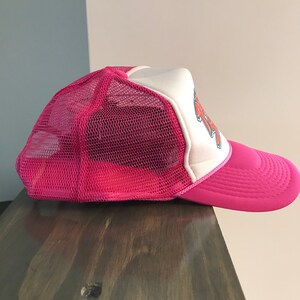 Op de afbeelding: Roze en witte mesh trucker cap met een rode en witte afbeelding aan de voorkant. De afbeelding zegt "Rock On".