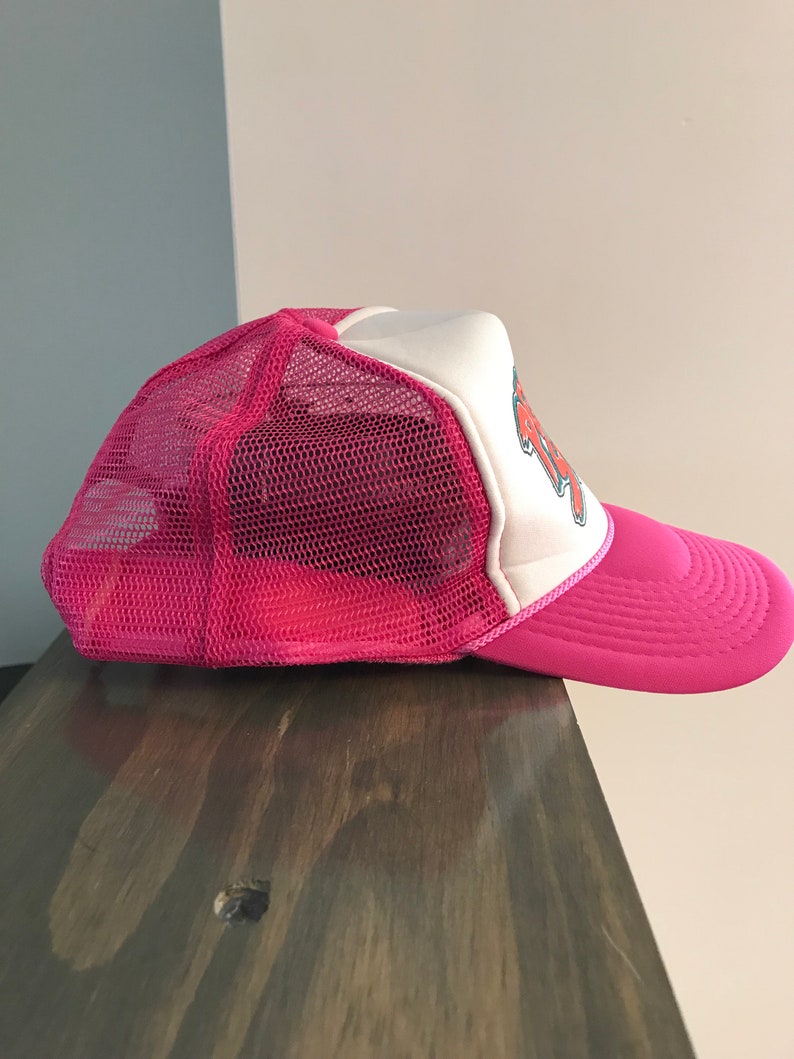 Op de afbeelding: Roze en witte mesh trucker cap met een rode en witte afbeelding aan de voorkant. De afbeelding zegt "Rock On".