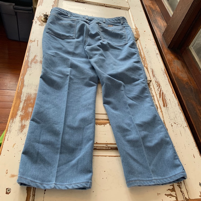 May include: A pair of light blue denim pants with a straight leg fit. The pants have a zipper fly and button closure. The back pockets are sewn on with a single stitch.