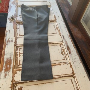 May include: A pair of gray dress pants with a subtle pinstripe pattern. The pants are folded and laid flat on a white wooden surface.
