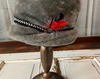 May include: A gray faux fur hat with a black and silver chain trim and a red feather accent.