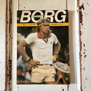 May include: A vintage magazine cover featuring Bjorn Borg. The cover has the word "BORG" in large white letters with a yellow stripe. The image shows a man in a white and red tennis outfit, holding a tennis racket and ball. The text "BY LARRY AUDETTE" is also visible.