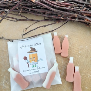 May include: A white paper bag with a sticker that says "Wizard Beer" and a cartoon wizard holding a beer mug. The sticker also says "Brewed under a full moon since 1895". There are five small, pink and white bottles of soap on the bag.