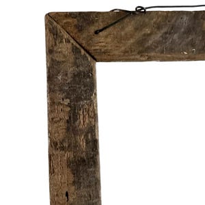 May include: A rectangular picture frame constructed from weathered, dark brown reclaimed wood with a visible grain and rough texture. The frame features mitered corners and a thin black metal wire attached to the top for hanging purposes.
