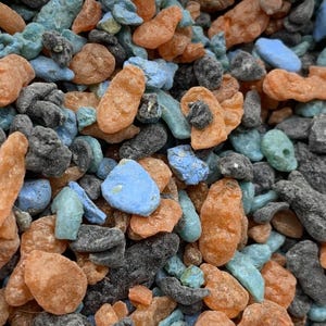 May include: Close-up of a collection of colorful, irregularly shaped resin pieces. The pieces are in shades of orange, blue, gray, and teal. The texture appears rough and uneven, with a slightly glossy finish.