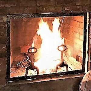 May include: A close-up of a fireplace with a fire burning inside. The fire is surrounded by a black metal frame. There are two black metal fireplace tools in the fire.