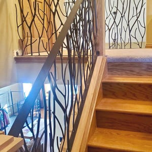 May include: A wooden staircase with a decorative metal railing. The railing features a black, tree branch-like design. The steps and wooden supports are a light brown color. The railing is on the left side of the stairs.