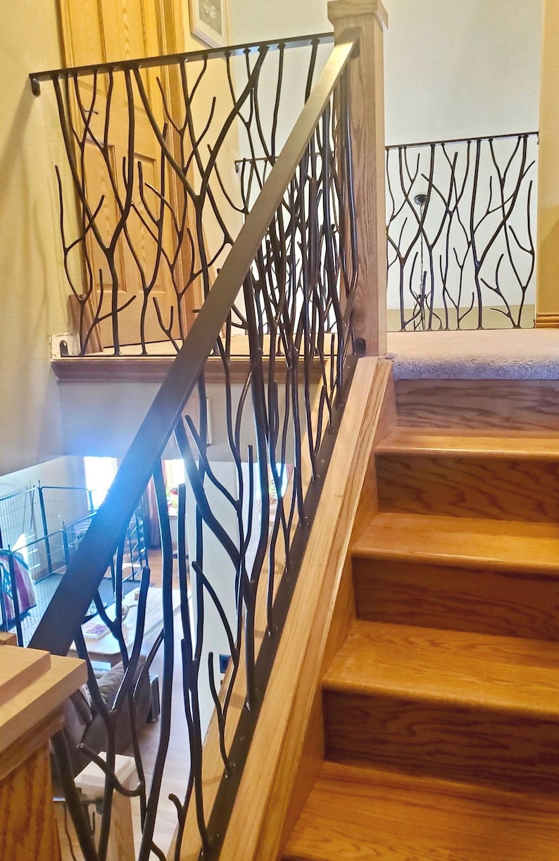 May include: A wooden staircase with a decorative metal railing. The railing features a black, tree branch-like design. The steps and wooden supports are a light brown color. The railing is on the left side of the stairs.