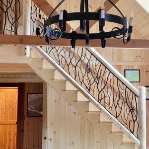 May include: A wooden staircase with a black metal railing featuring a tree branch design. The staircase is in a rustic-style home with a wooden ceiling and walls. A black chandelier hangs above the stairs.